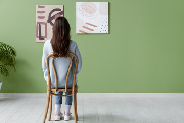 Young woman on chair looking at paintings in art gallery, back view