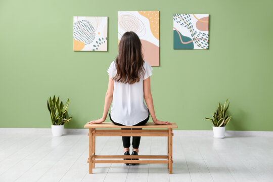 Young woman sitting on bench near paintings in art gallery, back view