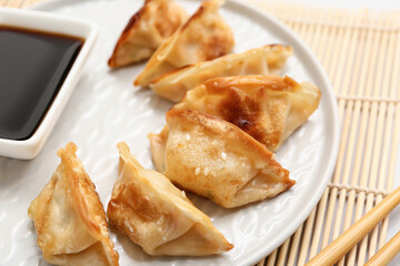 Plate of fried Japanese gyoza with sesame seeds and bowl of soy sauce on grey background, closeup