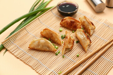 Fried Japanese gyoza with green onion and bowl of soy sauce on bamboo mat against yellow background