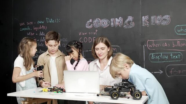 Caucasian teacher using laptop and explain about engineering system while diverse student holding electronic equipment in front of blackboard with prompt or code written in STEM class. Erudition.