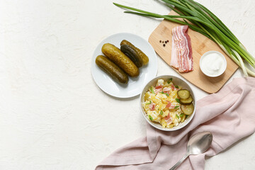 Bowl of tasty potato salad with bacon, green onion, sour cream and pickled cucumbers on white background