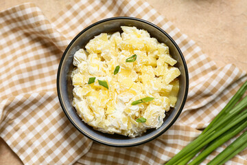 Bowl of tasty potato salad with green onion on beige grunge background