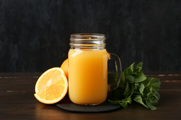 Mason jar of tasty juice with oranges and mint leaves on wooden table