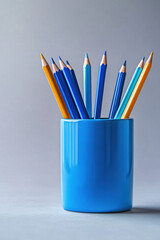 A collection of blue and yellow colored pencils standing upright in a matching blue container against a soft, neutral background.