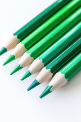 Close-up of green pencils arranged neatly against a white background, showcasing various shades and sharpened wooden tips.