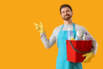 Male janitor with cleaning supplies pointing at something on yellow background