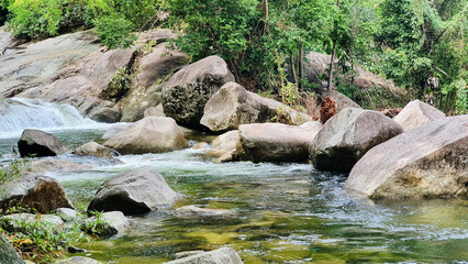 Landscape view from the middle of the stream flowing through the rocks, overlooking trees and mountains at Kiriwong Village, Nakhon Si Thammarat, Thailand