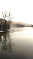 Sun rise in cold winter morning at river surrounded by trees reflecting in the still water