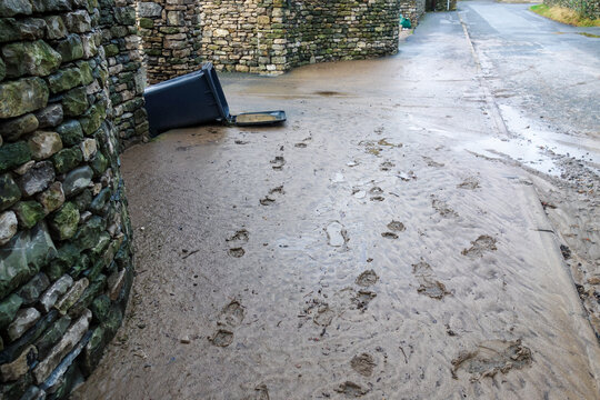 Knocked over waste wheely bin and footsteps in washed up river silt on a path after a big storm. 