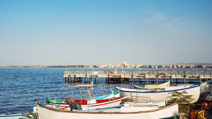 Obraz premium Pomorie. Brightly colored fishing boats are lined up along the shore, with a wooden pier extending into the serene sea. Bulgaria.