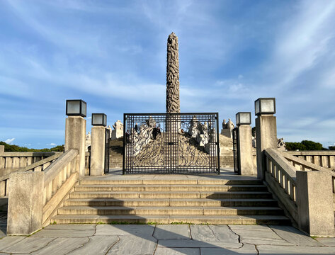 The entrance to Monolitten in Vigeland Park, Oslo, featuring a majestic wrought-iron gate with intricate designs, leading to the iconic sculpture surrounded by greenery.