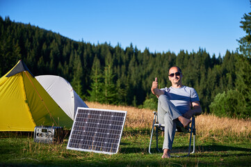 Man using photovoltaic solar panel for charging portable power station outdoor in eco-friendly...