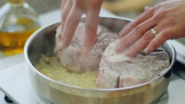 Crop woman chef braising ossobucco meat in a pan