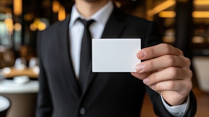 Fototapeta premium Corporate professional in formal attire holding a clean business card in front of a modern workspace design.