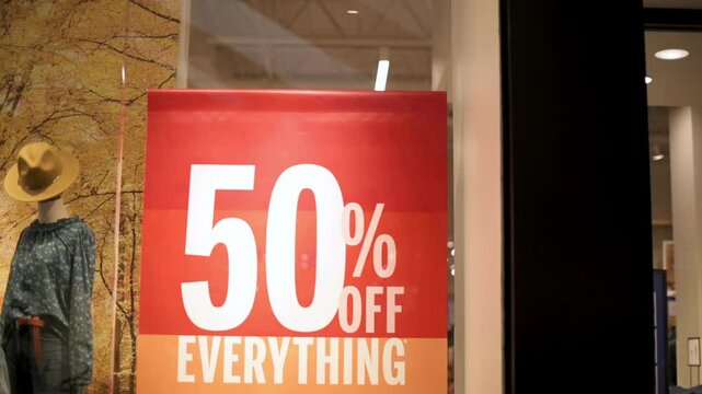 Bright red discount sign in retail window offering 50 off everything Mannequin display and fall-themed background create seasonal shopping atmosphere 50 off everything sale sign in storefront window