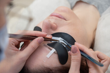 A woman undergoing eyelash extension procedure using an ultraviolet lamp.