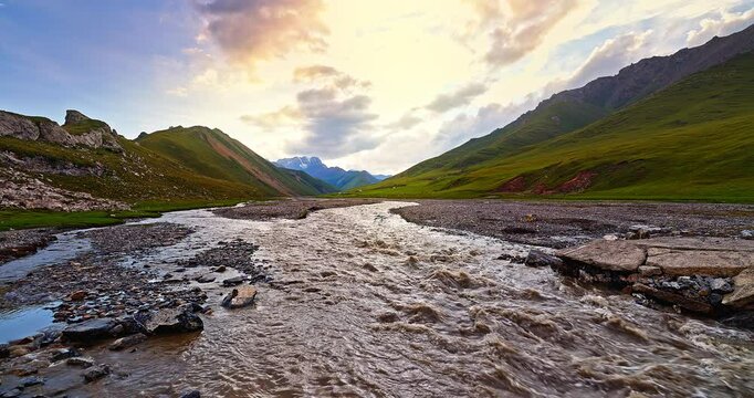 Flowing river and green grassland with mountain natural landscape at dusk. Beautiful scenery along the Duku Highway in Xinjiang, China.