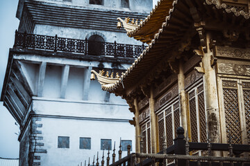 Ancient architecture in Dali, Yunnan, China.  A weathered white tower stands beside a richly...