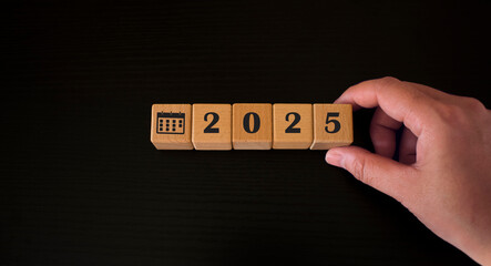 Woman holding wooden blocks with calendar icon and text "2025" placed on table. Goals, plans, intentions, strategies, plans, start, budget, mission, action, inspiration and new year concept.