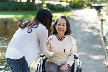 Asian senior woman in wheelchair with happy daughter. Family relationship retired woman sitting on wheelchair in the park age care at retirement home.