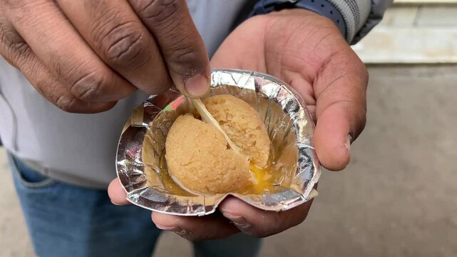 A boy slicing a nolen gur rosogolla in silver paper plate.