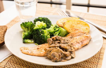 Fried river trout fillet with a complex side dish of broccoli, baked potatoes and mushroom sauce