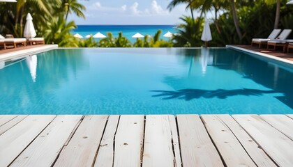 A vibrant view of a swimming pool with a clear blue water surface in the background. The foreground features a wooden countertop. In the distance, there are white umbrellas and palm trees , suggesting