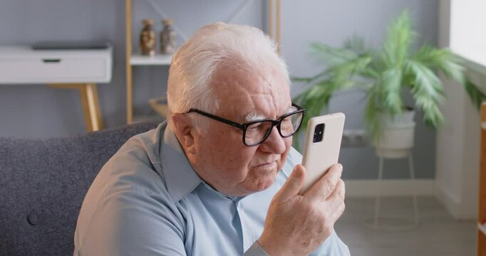 Senior man with poor eyesight is struggling to use the phone at home. Elderly individuals with disabilities and problems, highlighting the importance of accessibility and support for pensioners.
