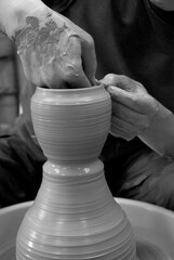 Hands are crafting pottery on a wheel, shaping wet clay into a tall form. The process reflects Japan’s rich tradition of ceramic art, blending skill and care in every movement.