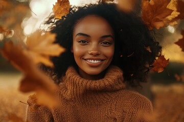 Young woman with beautiful curly hair smiles warmly amid falling autumn leaves, wrapped in cozy sweater, capturing the essence of seasonal joy and nature's beauty.