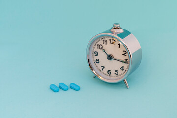 Alarm clock and blue pills on blue background. Sleep disorder and insomnia concept.