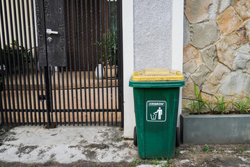 Green trash can on the front fence of the house