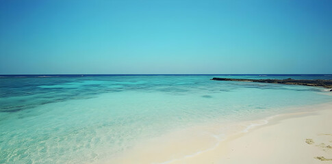 Obraz premium A serene beach view with clear turquoise waters and a cloudless blue sky.