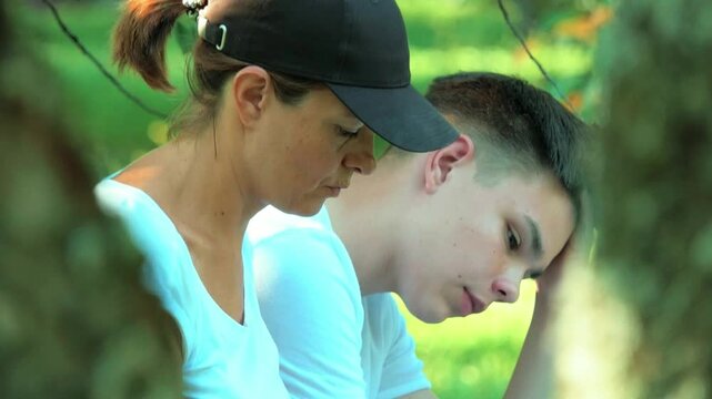 A woman and a teenager are sitting in a spring garden and doing their homework.