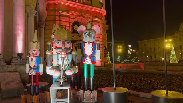 A view of a group of large, colorful nutcracker statues, including the Mouse King, displayed outdoors at night as part of the holiday decor.