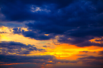 Dramatic sunset sky with vibrant orange and yellow tones blending into deep blue clouds, creating a striking contrast. Perfect for nature and atmospheric themes