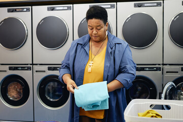 Medium full shot of senior African American woman folding clean and tidy clothes while checking...