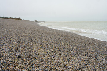 Rocky beach stretches along a calm shoreline under a cloudy sky in an expansive natural landscape