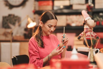 Dedicated to holiday spirit, a young woman skillfully decorates ornaments with bright colors while surrounded by festive decorations and a cozy atmosphere during Christmas