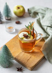 Homemade apple punch with fresh apples, cinnamon and rosemary in a cup on a light background