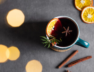 Mulled wine with orange, cinnamon and rosemary in a cup on a dark background with blur garlands.