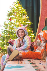 Christmas, New Year's photo. The children of a girl dressed as a unicorn and a fox cub are sitting on the couch, laughing, drinking milk and eating cookies.