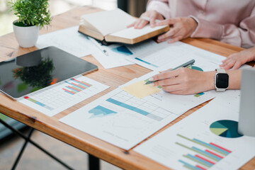 Professionals reviewing financial charts and graphs on a wooden desk, using digital devices and printed reports in a collaborative office environment.