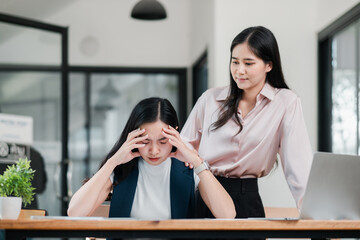 A businesswoman experiencing stress at her desk while a colleague offers support in a contemporary...