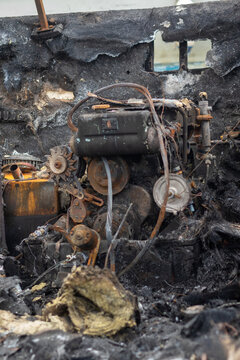 A burnt out engine in a boat wreck with ashes around = side view