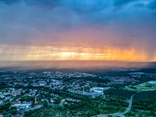 Rain Curtains at Sunset Over Polish City. A mesmerizing aerial view of rain curtains illuminated by a colorful sunset over a Polish city, blending urban structures with nature's dramatic sky.