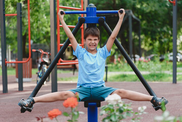 Happy boy doing sports on exercise machines on a summer playground. Children's exercises for health and concentration.