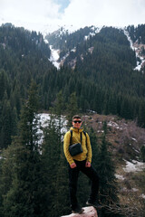 A young man in sunglasses stands against the backdrop of snow-capped mountain peaks. Trekking in the mountains