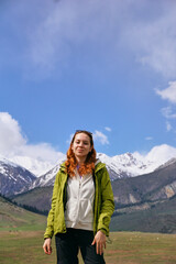 Naklejka premium A young girl in bright clothes smiles against the background of snowy peaks in a mountain valley